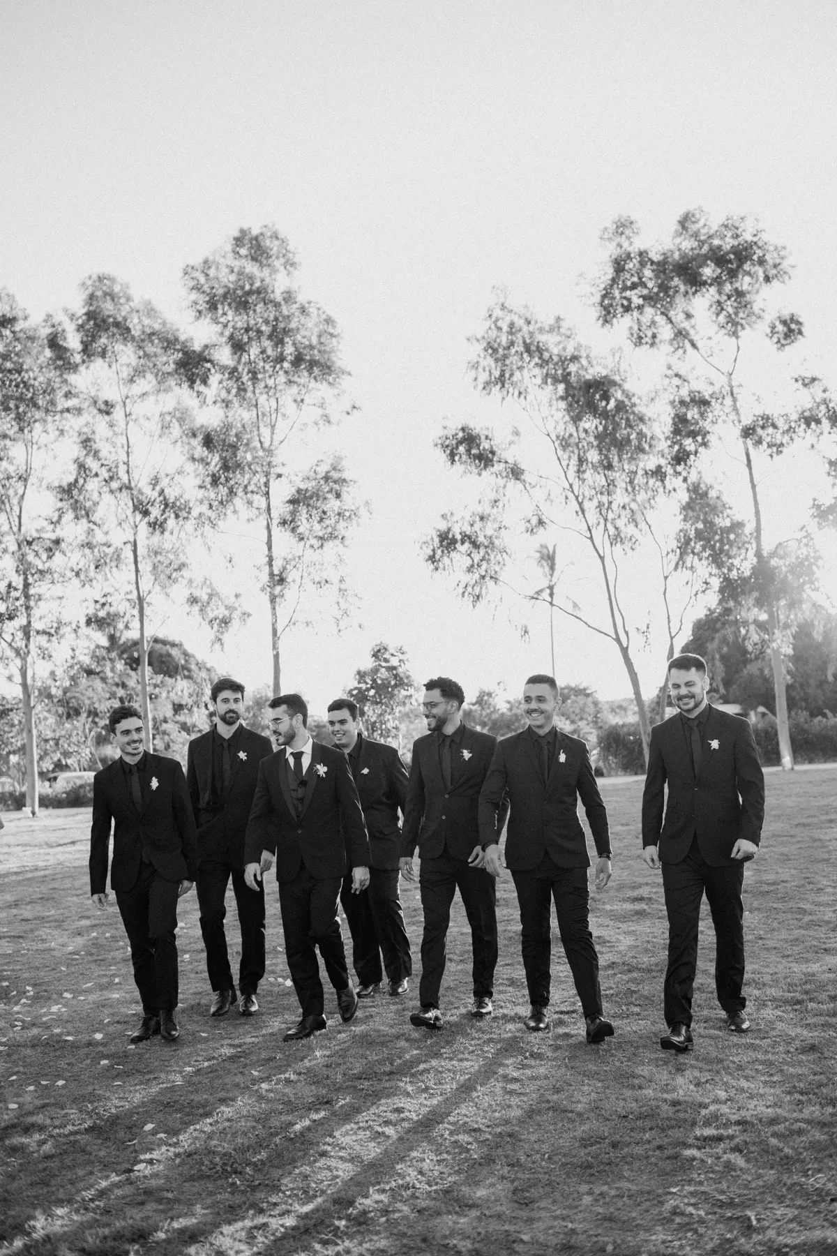 Noivo e padrinhos caminhando no gramado, em preto e branco